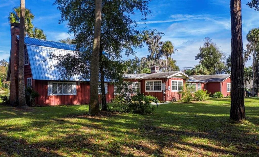 A red house with a metal roof and brick chimney sits on a grassy lot — 327 TANGLEWILDE STREET, APOPKA, FL