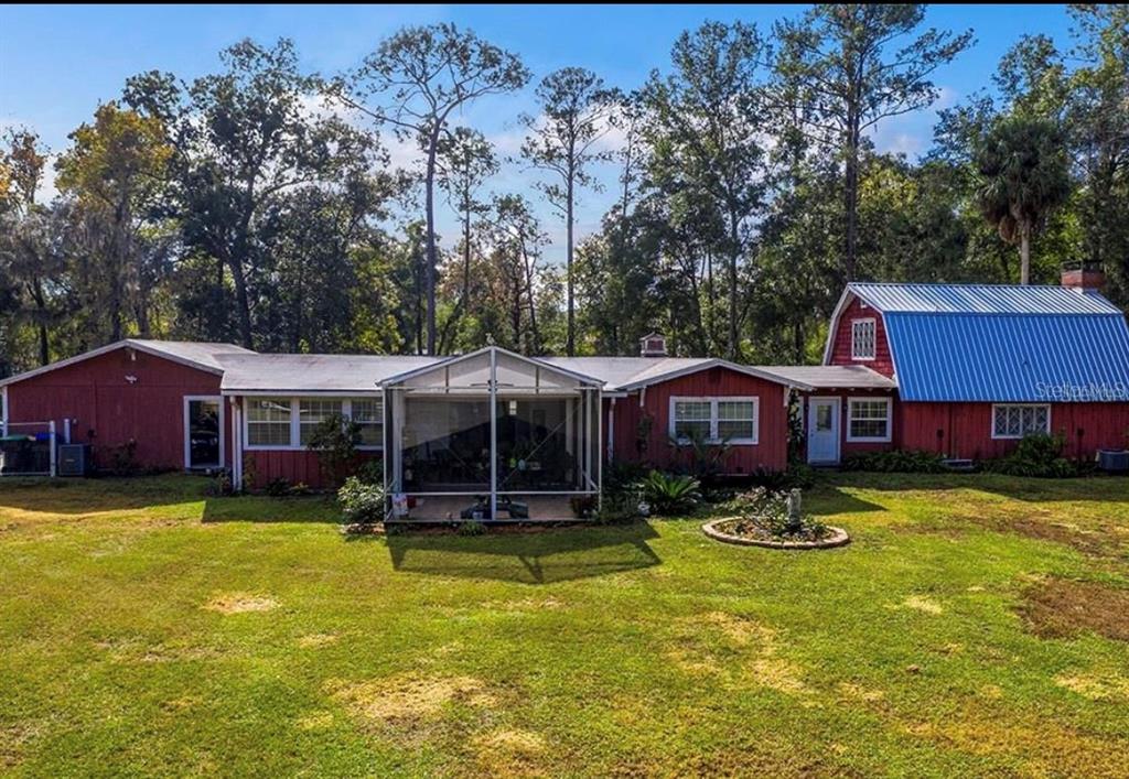 A red house with a metal roof and a screened-in porch sits on a grassy lot — 327 TANGLEWILDE STREET, APOPKA, FL