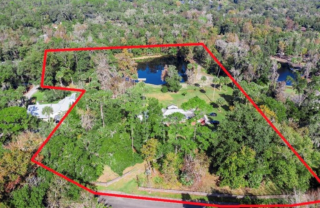 An aerial view shows a large, wooded residential lot with a pond and two houses — 327 TANGLEWILDE STREET, APOPKA, FL