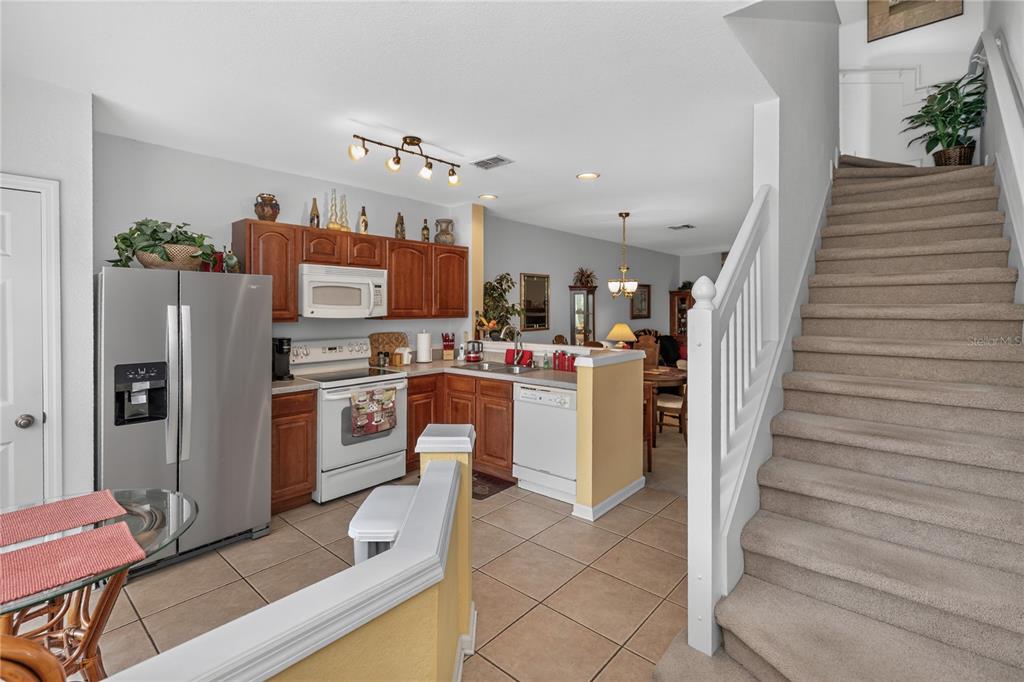 A kitchen with wood cabinets and stainless steel appliances sits beside a carpeted staircase — 716 SHROPSHIRE LOOP, SANFORD, FL