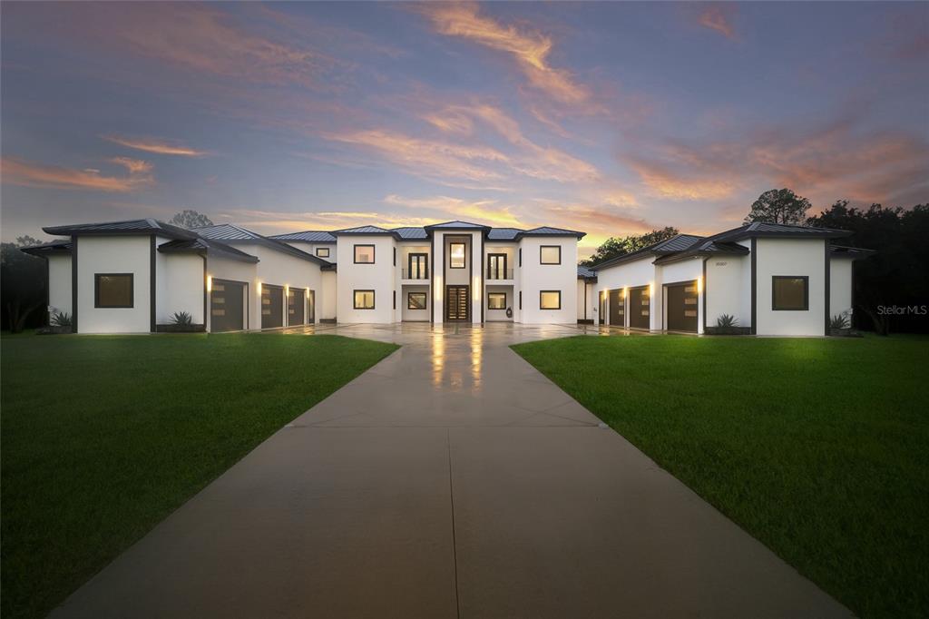A large, modern white house with a symmetrical facade and multiple garage bays at sunset — 20307 74TH AVENUE E, BRADENTON, FL