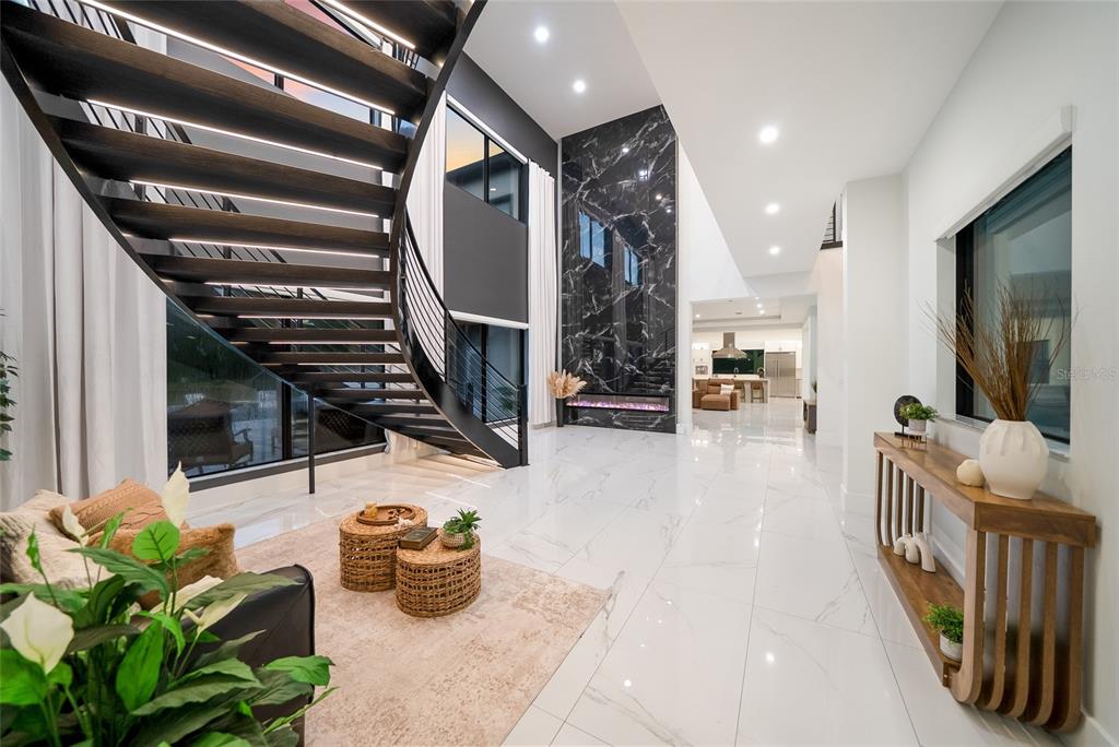 A modern living room features white marble floors, a black floating staircase, and floor-to-ceiling windows — 20307 74TH AVENUE E, BRADENTON, FL