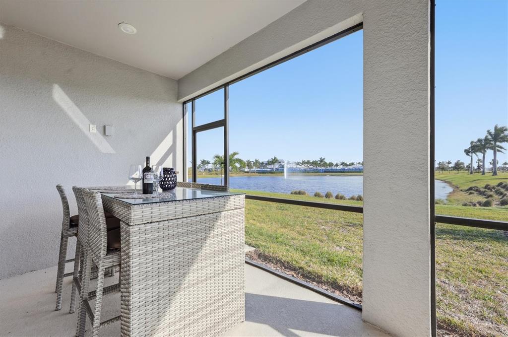 A screened-in patio features a wicker bar set overlooking a lake with a fountain — 8705 COASTAL KEY WAY, PARRISH, FL