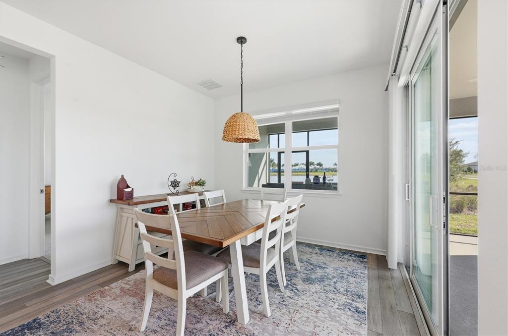 A dining room features a wooden table, white chairs, a woven pendant light, and rug — 8705 COASTAL KEY WAY, PARRISH, FL