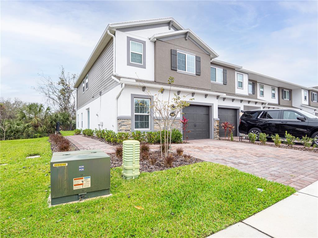 A two-story townhouse with a stone-accented facade, a paved driveway, and a green utility box — 4902 LIVINGSTON LANE, OVIEDO, FL