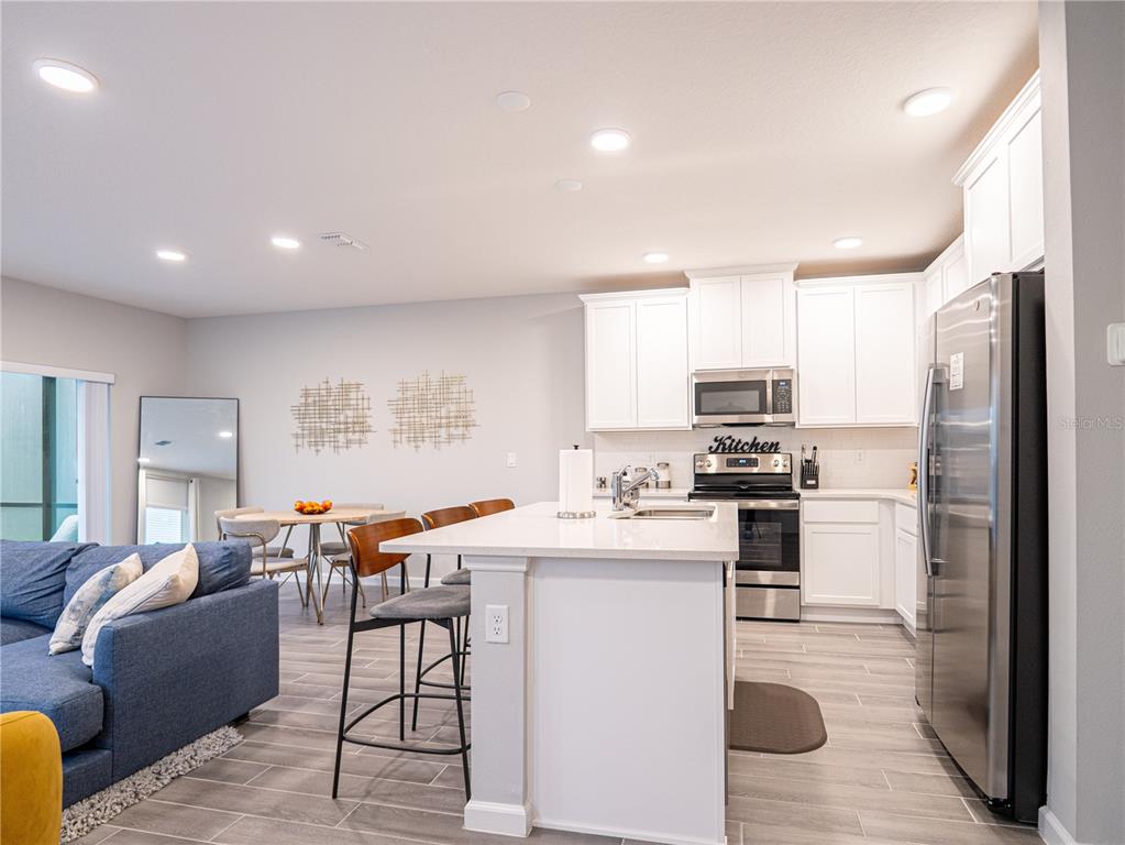 A modern kitchen features white cabinetry, stainless steel appliances, and a central island with seating — 4902 LIVINGSTON LANE, OVIEDO, FL