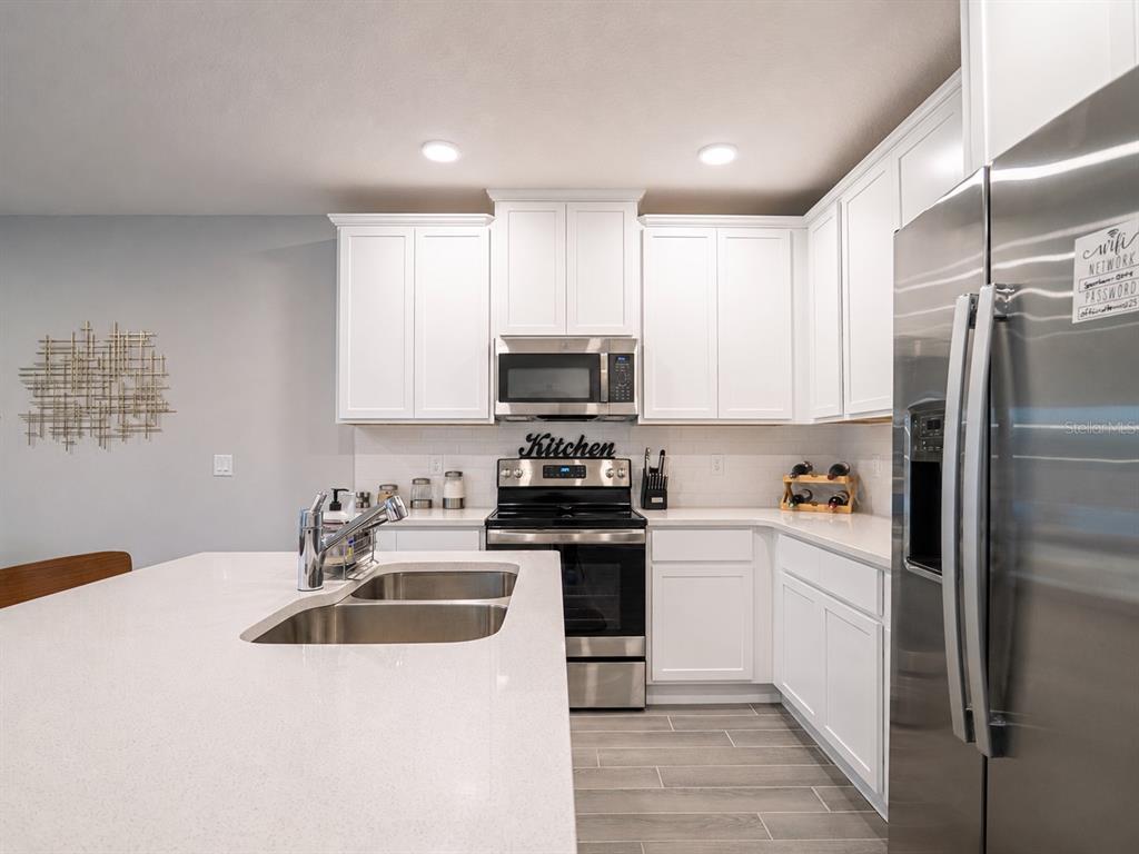 A modern kitchen features white cabinets, stainless steel appliances, and a large quartz island — 4902 LIVINGSTON LANE, OVIEDO, FL