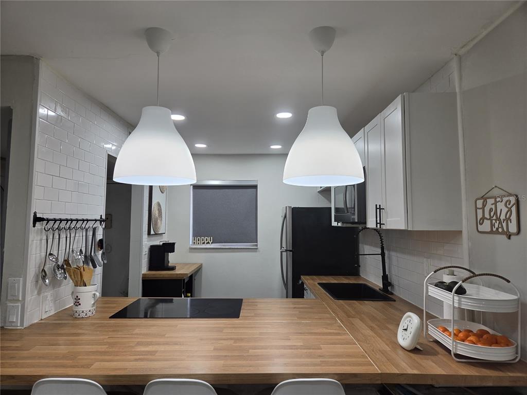A kitchen features a wooden countertop island, white pendant lights, and white subway tile walls — 2850 N POWERS DRIVE UNIT 83, ORLANDO, FL