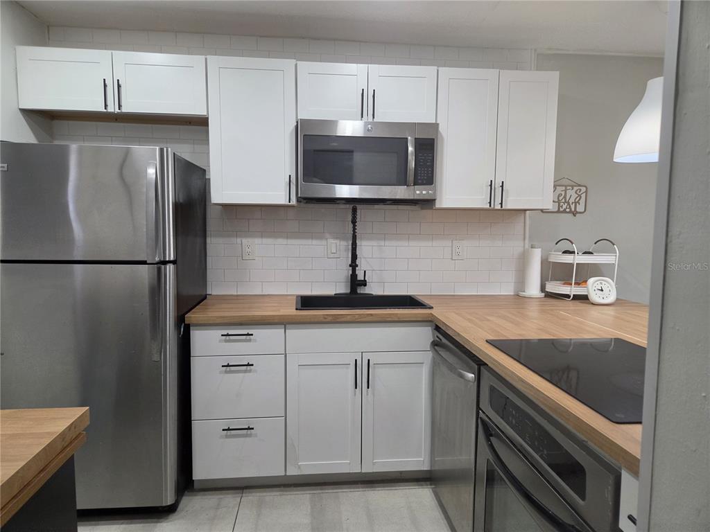 A kitchen features white cabinets, stainless steel appliances, a black sink, and wood countertops — 2850 N POWERS DRIVE UNIT 83, ORLANDO, FL