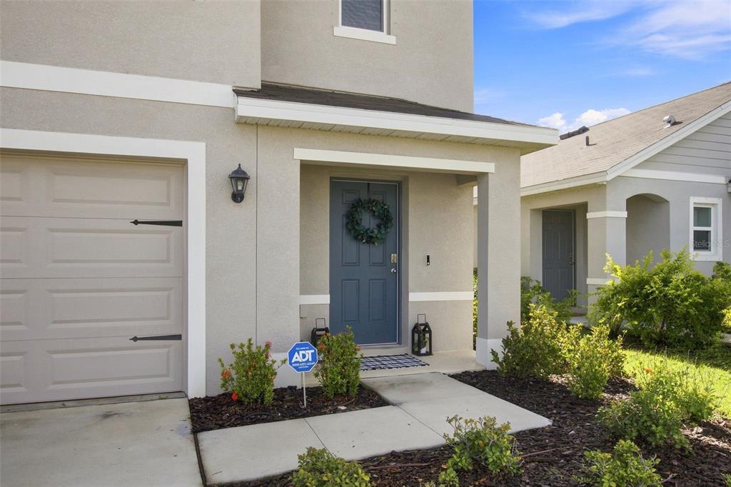 A beige house exterior features a blue front door, a garage, and a small garden — 6118 DISTANT HAZE PLACE, PALMETTO, FL