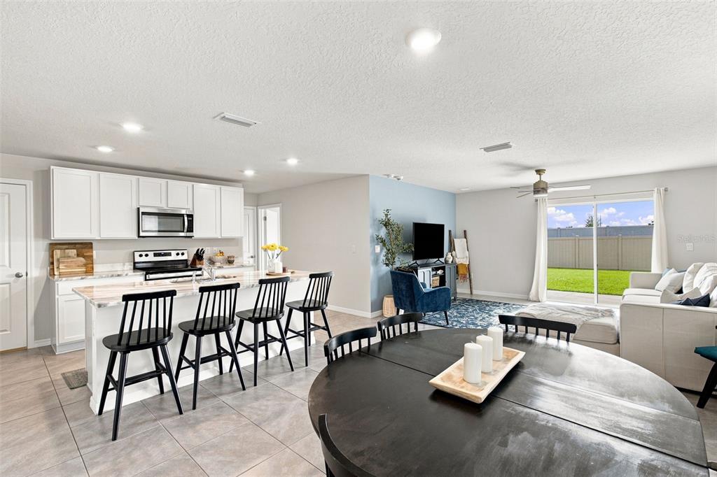 An open-concept kitchen, dining area, and living room with tile flooring and sliding glass doors — 6118 DISTANT HAZE PLACE, PALMETTO, FL