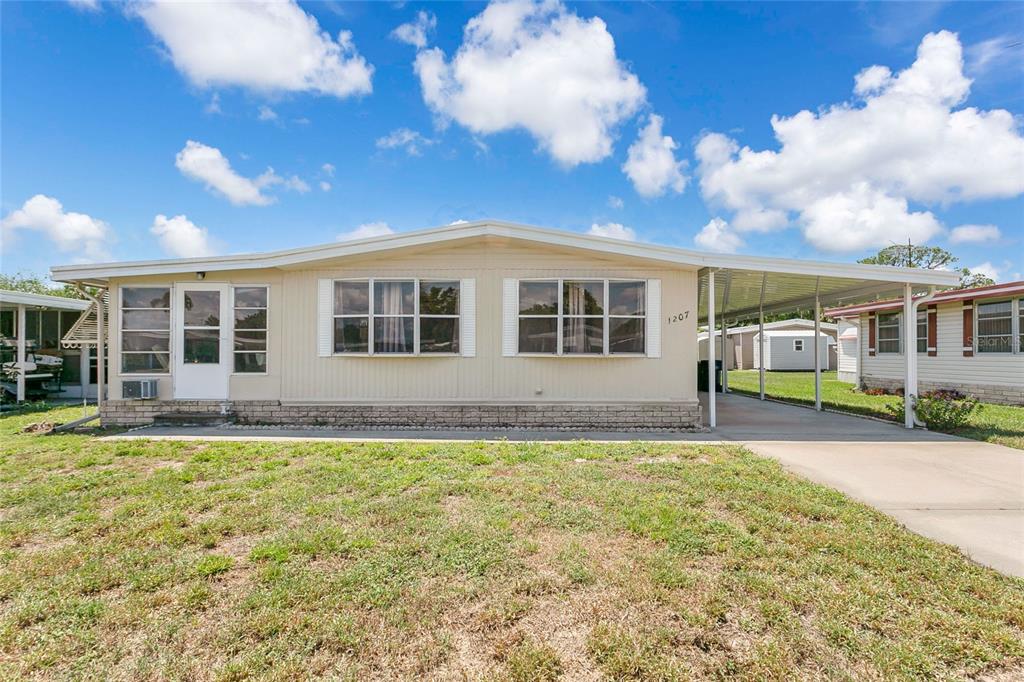 An aerial view shows a single-story manufactured home with a white roof and concrete driveway — 1207 APACHE CIRCLE, TAVARES, FL