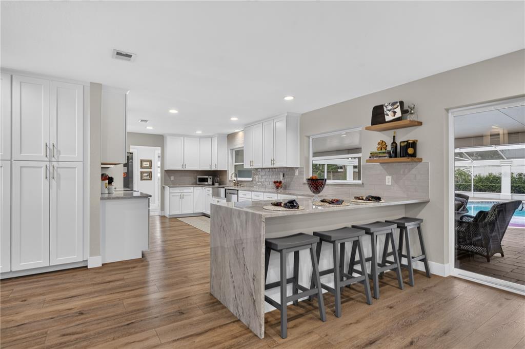 A modern kitchen features white cabinetry, a marble-topped island with bar stools, and wood flooring — 165 LAKE DESTINY TRAIL, ALTAMONTE SPRINGS, FL