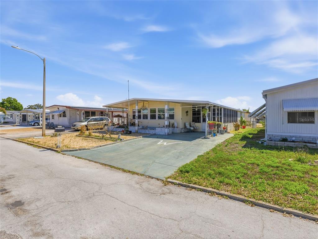 A light yellow mobile home with a carport and a paved driveway under a blue sky — 7402 CASCADE DRIVE, HUDSON, FL