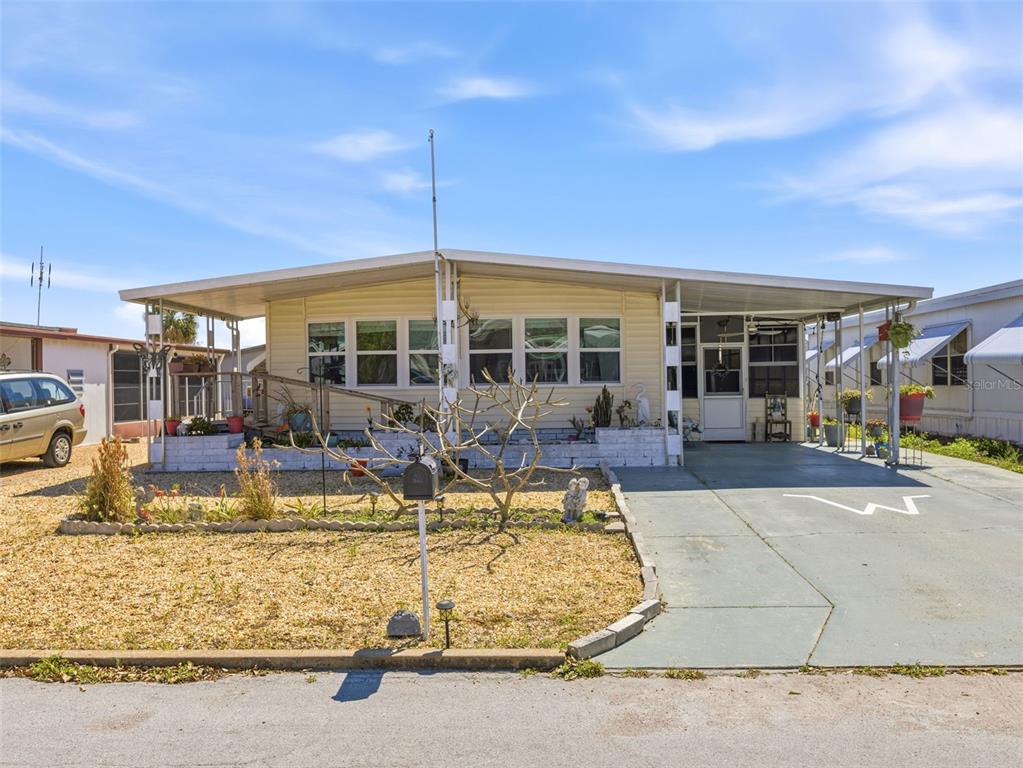 A single-story manufactured home with a gravel front yard, a concrete driveway, and a carport — 7402 CASCADE DRIVE, HUDSON, FL
