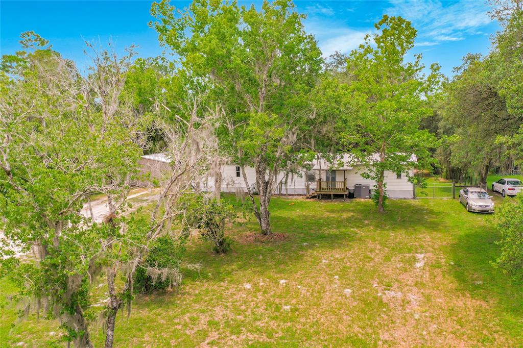 A single-story manufactured home sits on a grassy lot surrounded by large, mossy trees — 31032 RORY LANE, EUSTIS, FL
