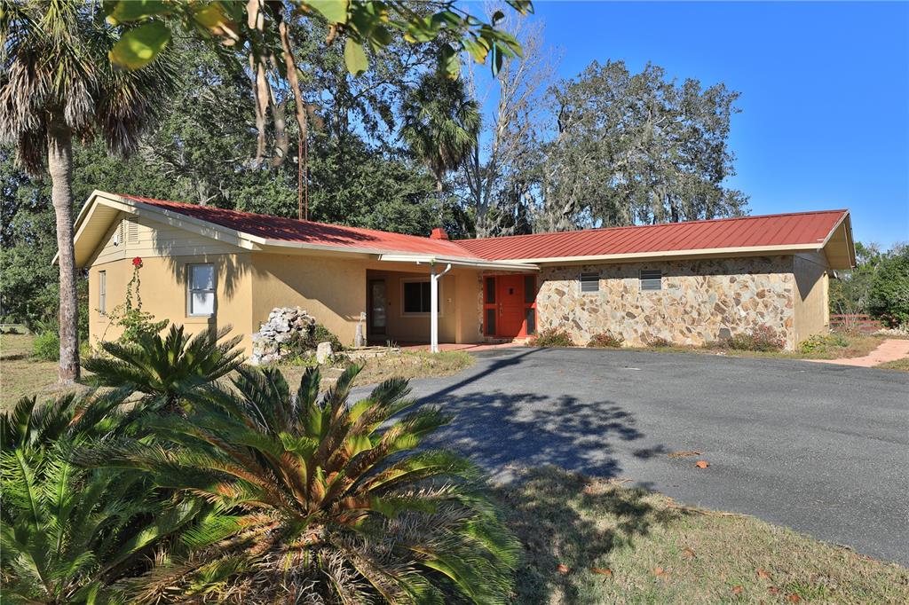 A single-story house with a red metal roof, stone facade, and a paved driveway — 2155 SE COUNTY HIGHWAY 484, BELLEVIEW, FL