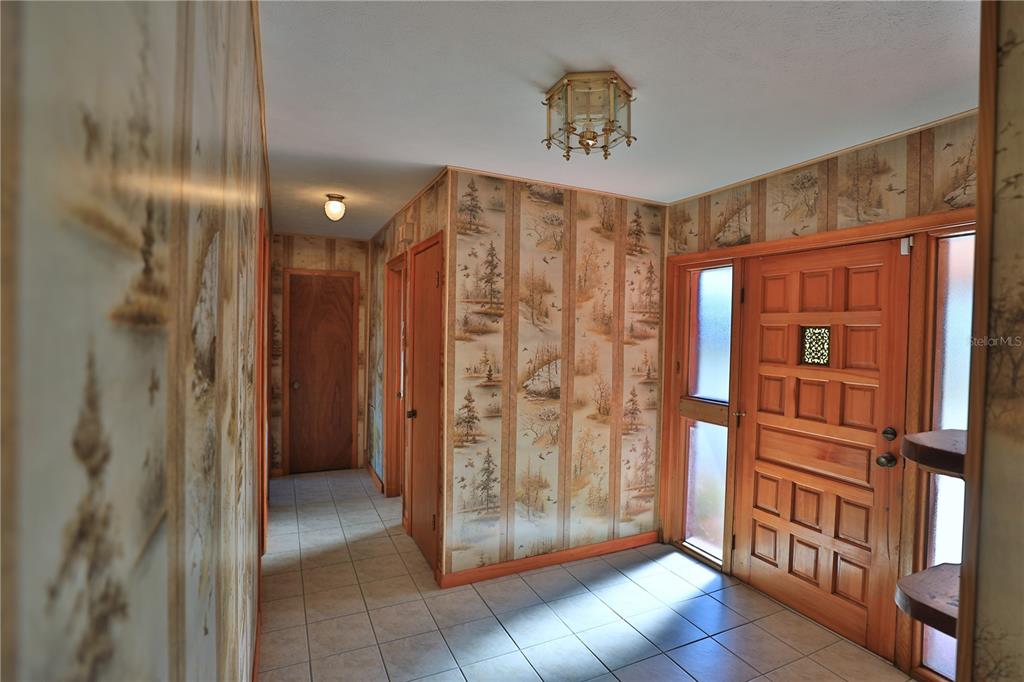 An entryway features tiled flooring, wood-paneled doors, and wallpaper depicting a forest scene — 2155 SE COUNTY HIGHWAY 484, BELLEVIEW, FL