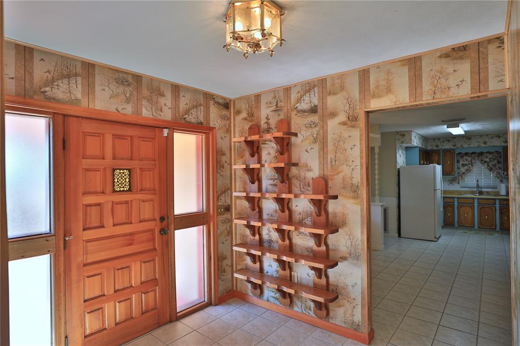 An entryway features wood-paneled wallpaper, a wooden front door, and a wall-mounted tiered shelving unit — 2155 SE COUNTY HIGHWAY 484, BELLEVIEW, FL