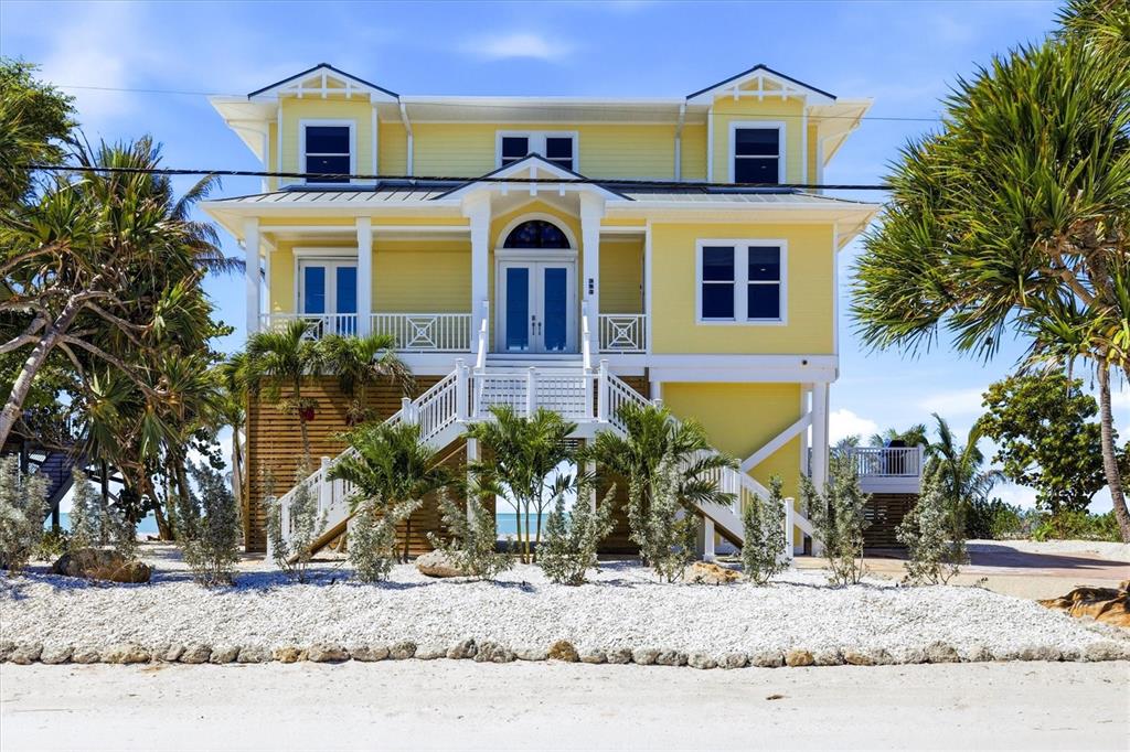 A yellow two-story house on stilts features a central staircase leading to the front entrance — 131 S GULF BOULEVARD, PLACIDA, FL