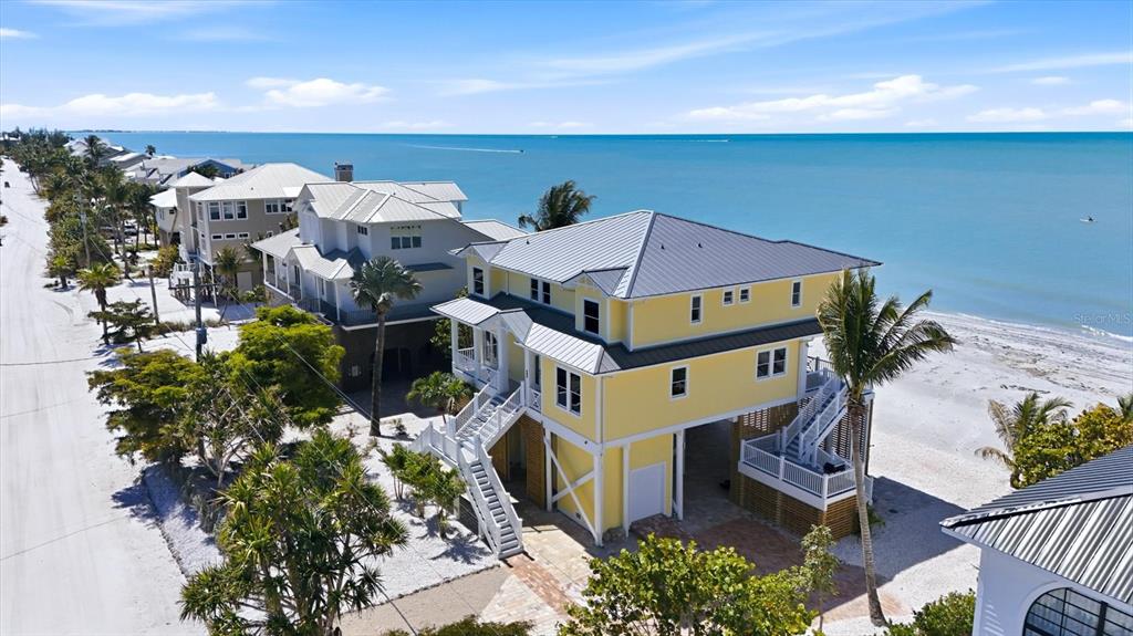 An elevated yellow house with a metal roof sits on a sandy beach — 131 S GULF BOULEVARD, PLACIDA, FL