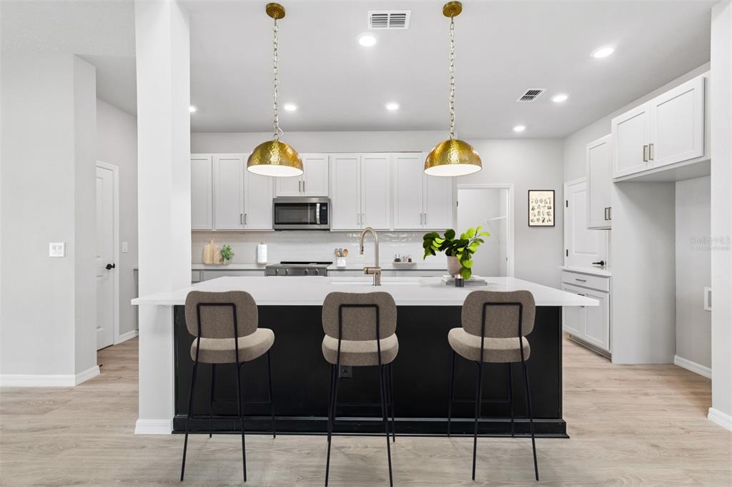 A modern kitchen features a black island with three stools, white cabinets, and gold pendant lights — 15239 EASTLYN DRIVE, BRADENTON, FL