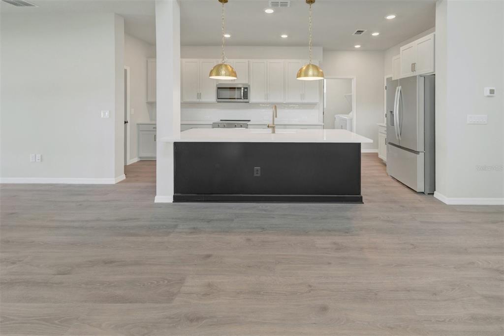 A modern kitchen features a dark island, white cabinetry, stainless steel appliances, and wood flooring — 15239 EASTLYN DRIVE, BRADENTON, FL