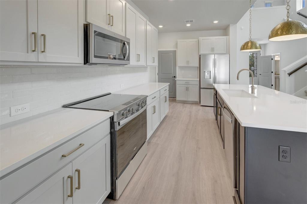 A modern kitchen features white cabinets, stainless steel appliances, a kitchen island, and light flooring — 15239 EASTLYN DRIVE, BRADENTON, FL