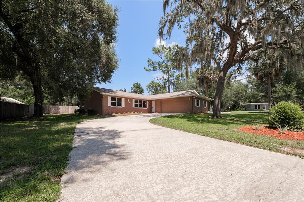 A single-story brick house with a concrete driveway and large oak trees in the yard — 34691 ORCHID PARKWAY, DADE CITY, FL