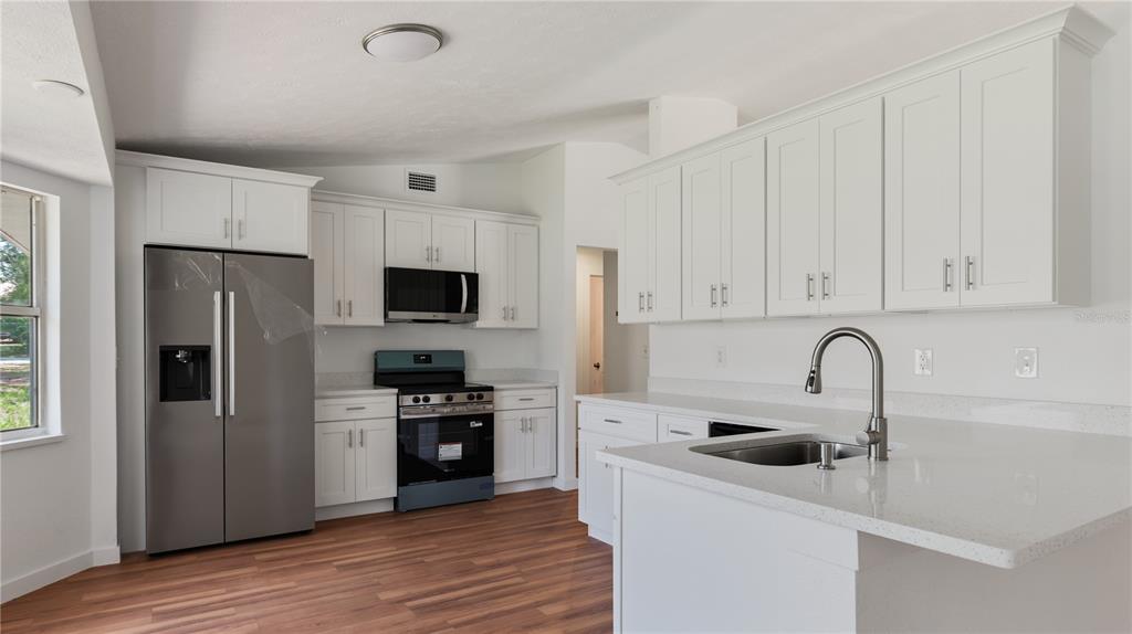 A kitchen features white cabinets, stainless steel appliances, and light-colored countertops with a sink — 34691 ORCHID PARKWAY, DADE CITY, FL