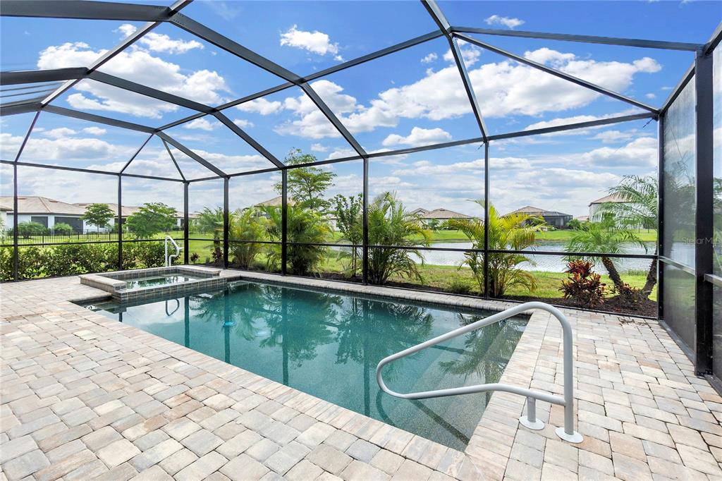 A screened-in patio features a rectangular swimming pool, a small hot tub, and paver flooring — 5239 CORAL REEF WAY, BRADENTON, FL