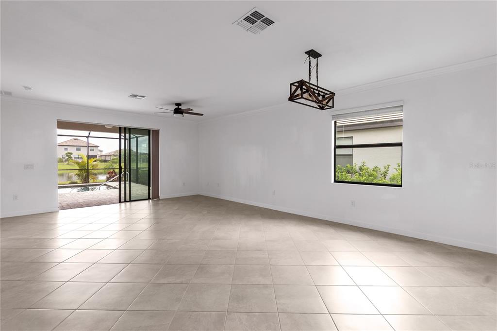 A spacious, white-walled living room features large beige floor tiles, a chandelier, and sliding doors — 5239 CORAL REEF WAY, BRADENTON, FL