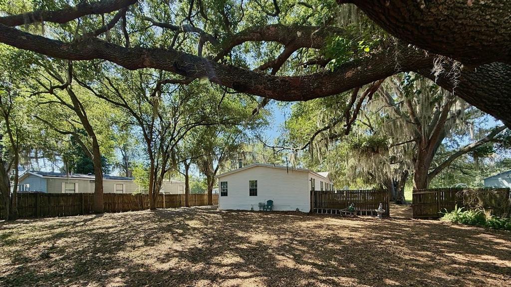 A white house sits in a large, shaded yard surrounded by a wooden fence — 4817 ROLLINGLEN LOOP W, LAKELAND, FL