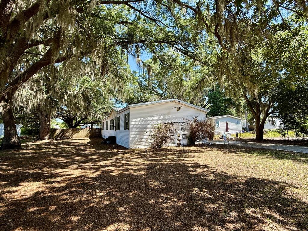 A white mobile home sits on a shaded lot with large oak trees — 4817 ROLLINGLEN LOOP W, LAKELAND, FL