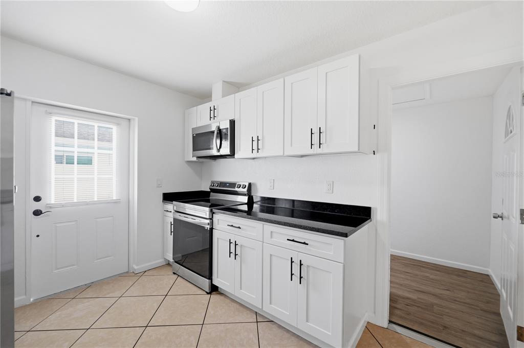 A kitchen features white cabinets, black countertops, stainless steel appliances, and light-colored tile flooring — 1514 BURNING TREE LANE, BRANDON, FL