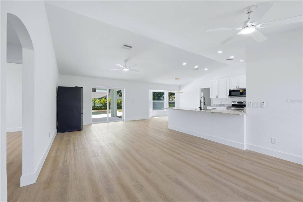An open-concept living area features light wood-look flooring, a kitchen island, and white walls — 27215 PUNTA CABELLO COURT, PUNTA GORDA, FL