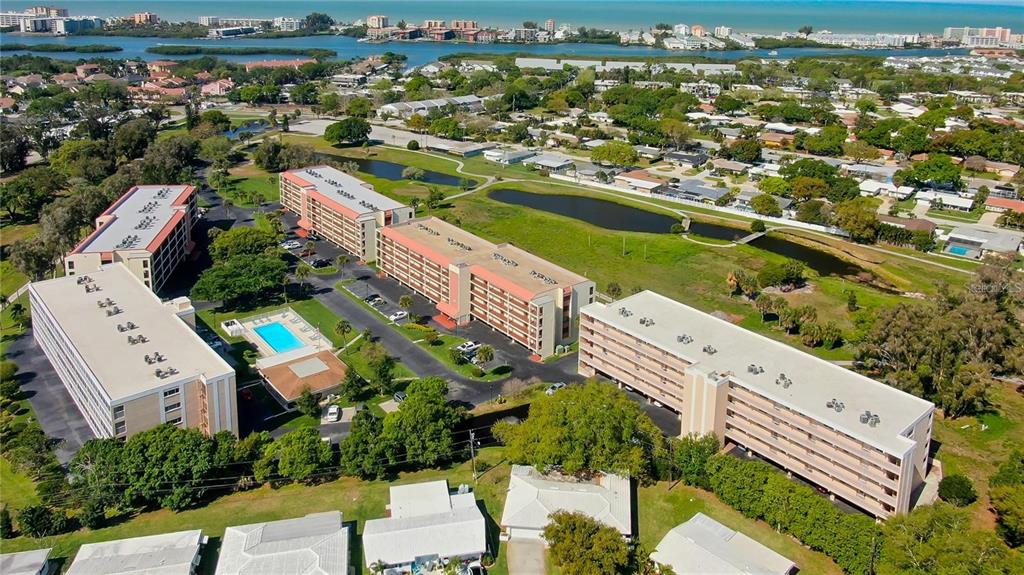An aerial view shows several multi-story apartment buildings surrounded by green space and a pool — 9433 HARBOR GREENS WAY UNIT 404, SEMINOLE, FL