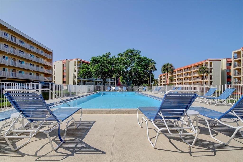 A swimming pool surrounded by lounge chairs in a courtyard between multi-story apartment buildings — 9433 HARBOR GREENS WAY UNIT 404, SEMINOLE, FL