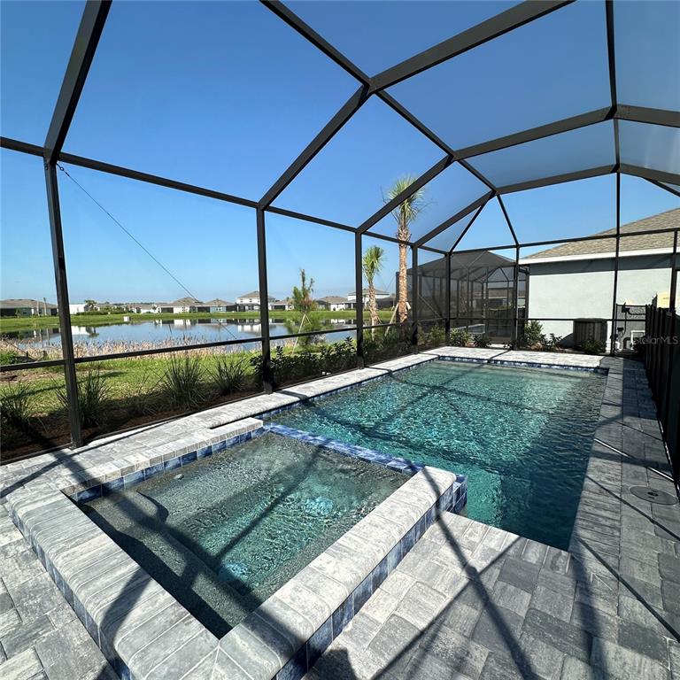 A screened-in pool and spa area with paver decking overlooking a pond — 3613 AMBERSWEET CROSSING, PARRISH, FL