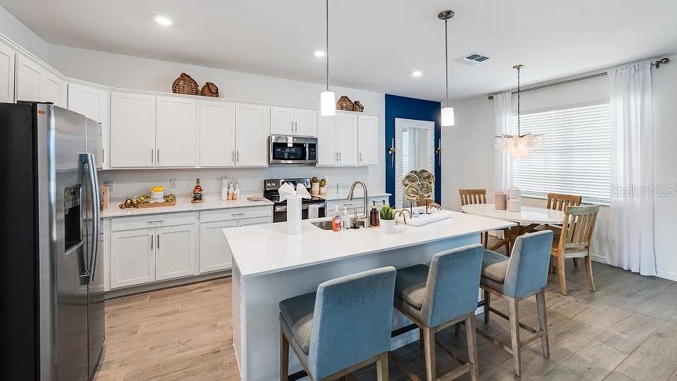 A modern kitchen features white cabinetry, a large central island, and an adjacent dining area — 3613 AMBERSWEET CROSSING, PARRISH, FL