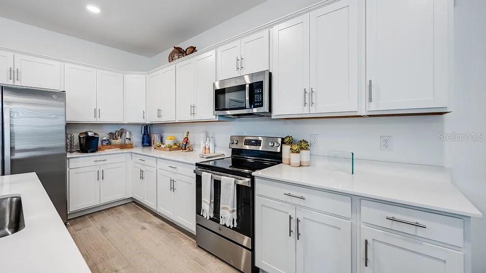 A modern kitchen features white cabinets, stainless steel appliances, and light wood-look flooring — 3613 AMBERSWEET CROSSING, PARRISH, FL
