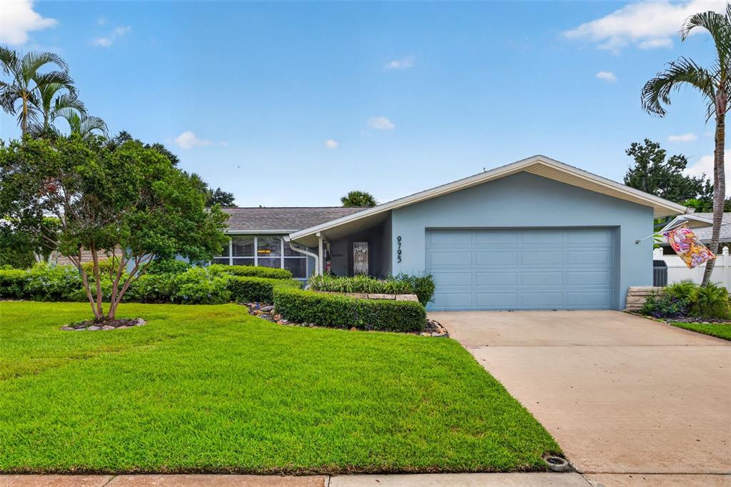 A single-story house with a blue exterior, a two-car garage, and a manicured front lawn — 9795 PORTSIDE DRIVE, SEMINOLE, FL