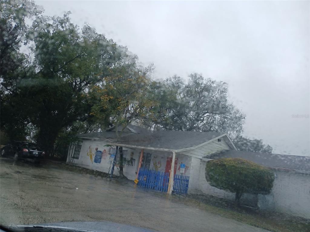 A single-story building with a white exterior, a blue fence, and a large tree nearby — 2203 US-17, BARTOW, FL