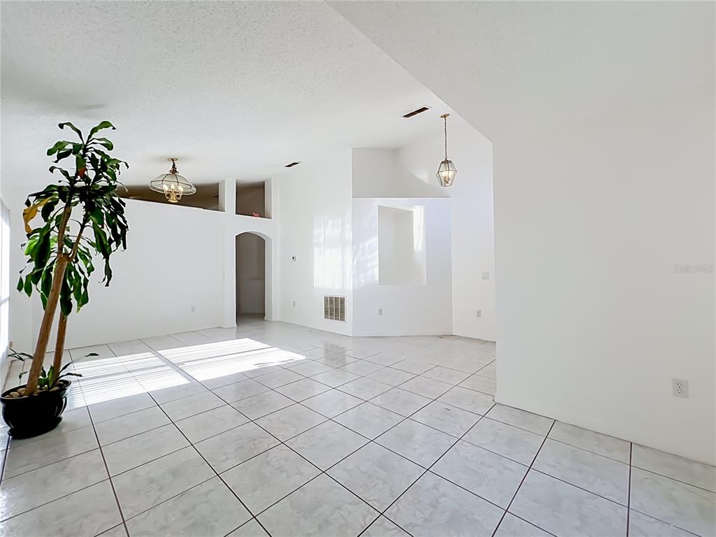A bright, empty room features white walls, tiled floors, a potted plant, and two light fixtures — 11781 HATCHER CIRCLE, ORLANDO, FL