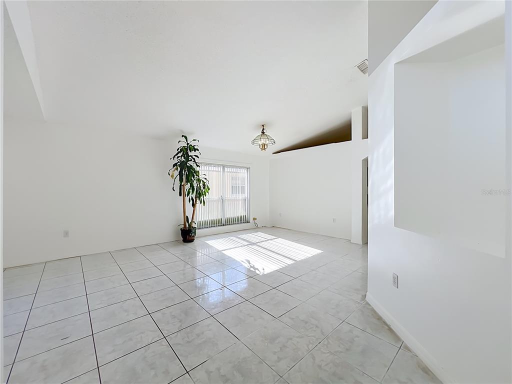 An empty room features white walls, light-colored tile flooring, a large window, and a potted plant — 11781 HATCHER CIRCLE, ORLANDO, FL
