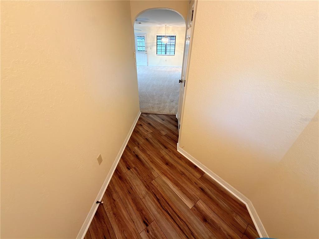 A hallway with wood-look flooring leads to a white front door under an arched entryway — 1241 SHAMROCK DRIVE, SEBRING, FL