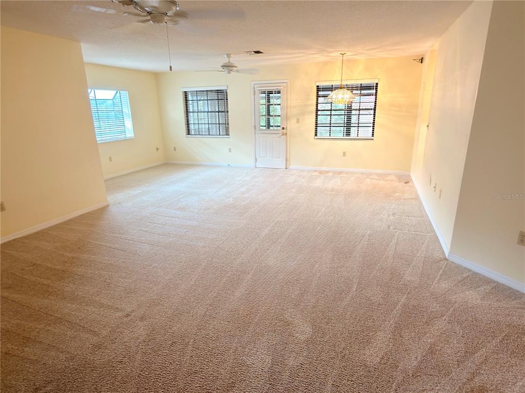A spacious room with beige carpeting, light yellow walls, two ceiling fans, and a door — 1241 SHAMROCK DRIVE, SEBRING, FL