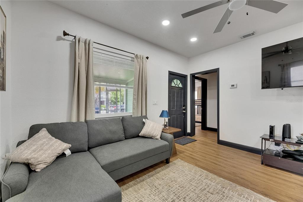 A living room features a gray sectional sofa, wood-look flooring, and a wall-mounted television — 1009 E COLUMBUS DRIVE, TAMPA, FL