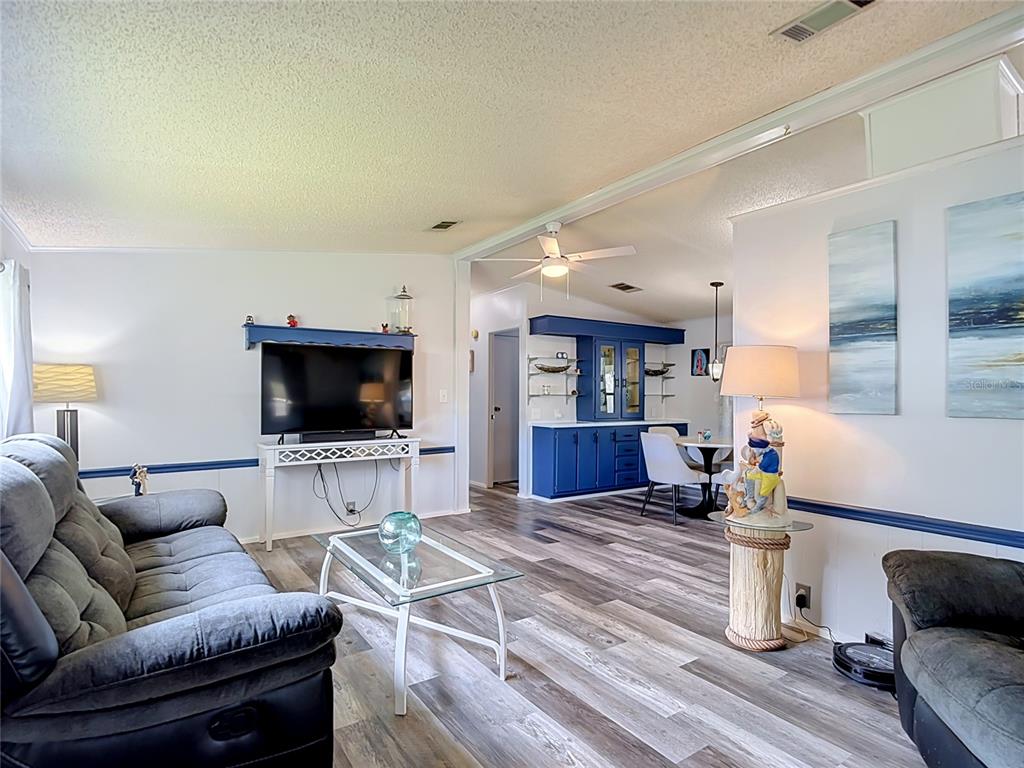 An open-concept kitchen and living area features blue cabinets, a round dining table, and flooring — 4616 OLIVE DRIVE, ZEPHYRHILLS, FL
