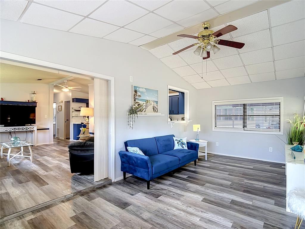 A living room with wood-look flooring, a blue sofa, and a drop ceiling with a fan — 4616 OLIVE DRIVE, ZEPHYRHILLS, FL